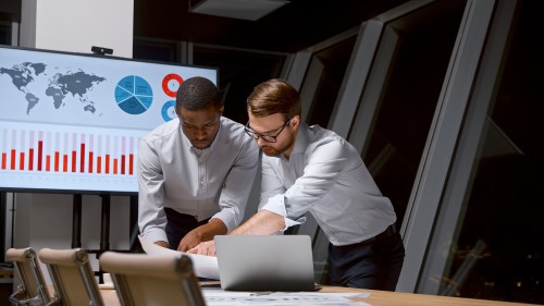 Two businessmen working in a team doing analytics in the office after a working day