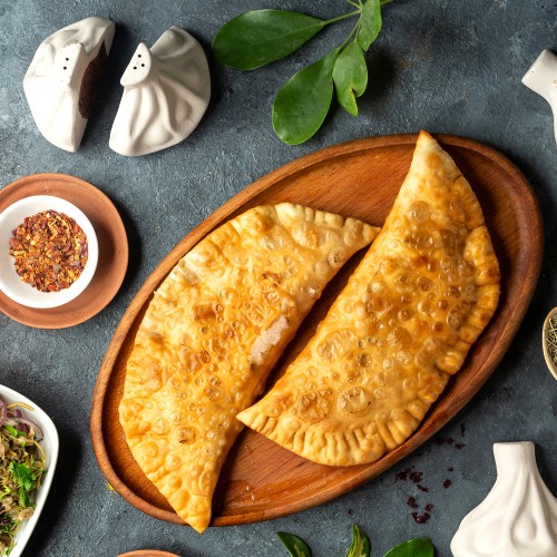 top view of homemade meat pies belyashi on a wooden platter on dark background